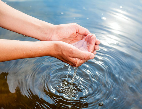 Imagen de manos recogiendo agua limpia desde una corriente de agua